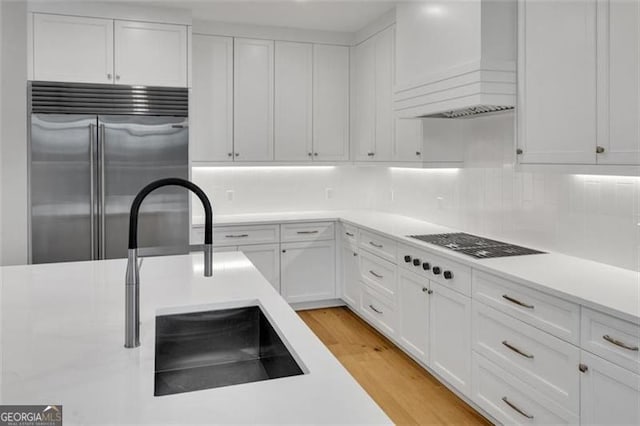 kitchen featuring built in refrigerator, custom range hood, white cabinetry, and light countertops