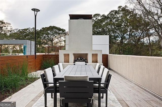 view of patio featuring exterior fireplace, outdoor dining space, and fence
