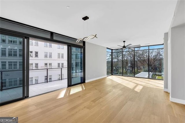 unfurnished living room with wood finished floors, ceiling fan, baseboards, and floor to ceiling windows