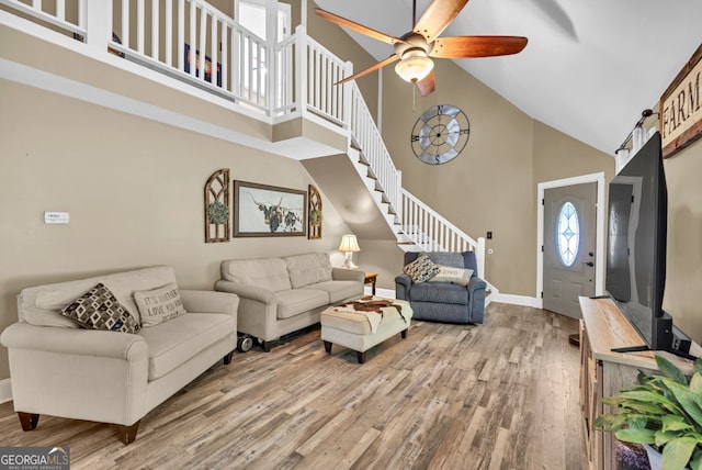 living room with high vaulted ceiling, stairs, wood finished floors, a ceiling fan, and baseboards