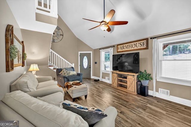 living area with stairway, a ceiling fan, baseboards, wood finished floors, and high vaulted ceiling