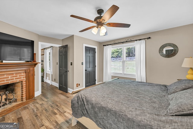 bedroom with wood finished floors, baseboards, a brick fireplace, and ceiling fan