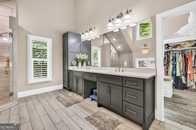 bathroom featuring wood finished floors, high vaulted ceiling, a tile shower, plenty of natural light, and vanity