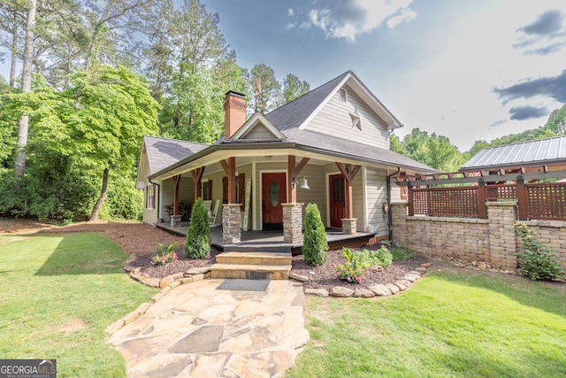 view of front of property featuring a chimney, a front lawn, covered porch, and roof with shingles
