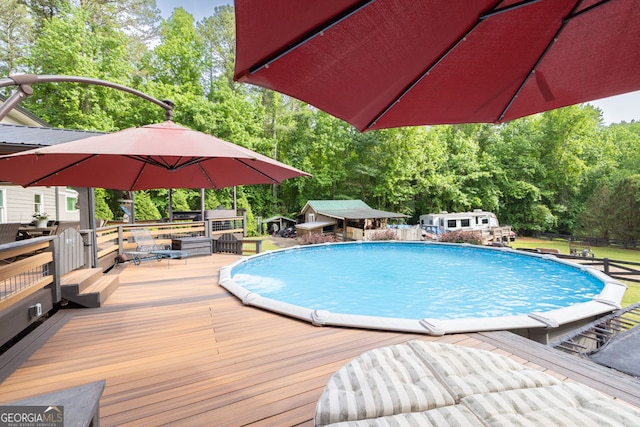swimming pool with a wooden deck, an outdoor structure, and view of wooded area