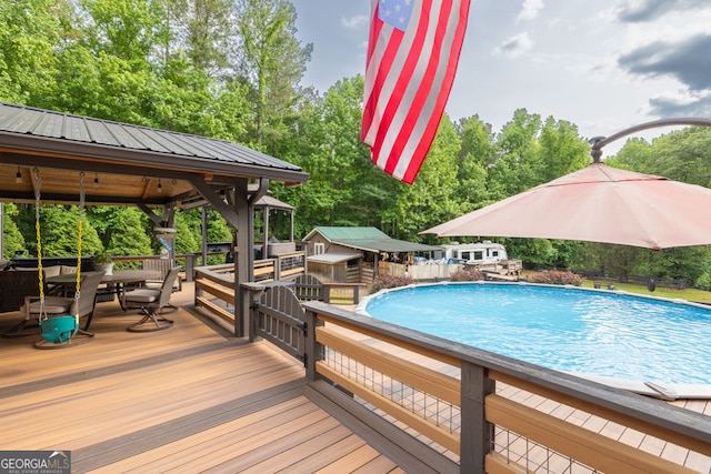 swimming pool with outdoor dining space, a wooden deck, a gazebo, and view of wooded area