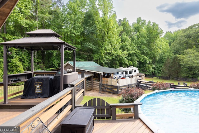 wooden deck featuring an outdoor pool, a gazebo, fence, and view of wooded area