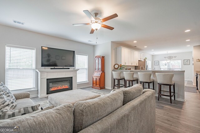 living room with baseboards, a ceiling fan, wood finished floors, a chandelier, and recessed lighting