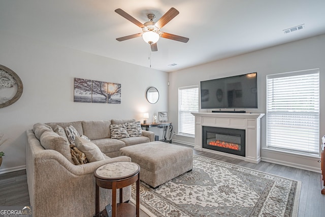living room featuring ceiling fan, wood finished floors, baseboards, and a glass covered fireplace
