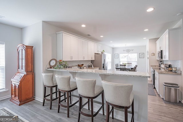 kitchen featuring stainless steel appliances, backsplash, a peninsula, white cabinetry, and light wood finished floors