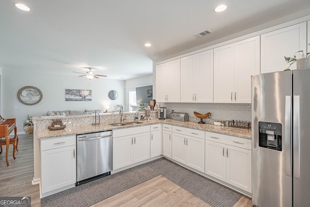 kitchen featuring stainless steel appliances, a sink, a peninsula, light wood-style flooring, and white cabinetry