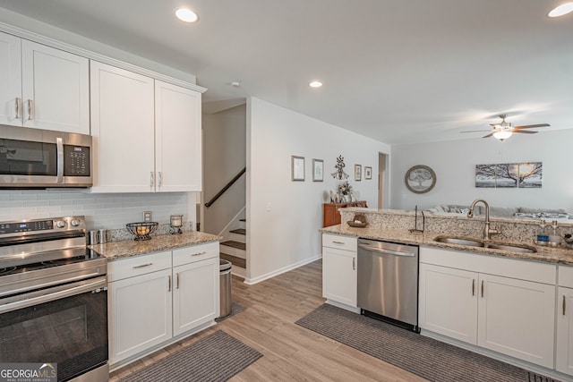 kitchen featuring appliances with stainless steel finishes, a sink, light wood-style flooring, backsplash, and a ceiling fan