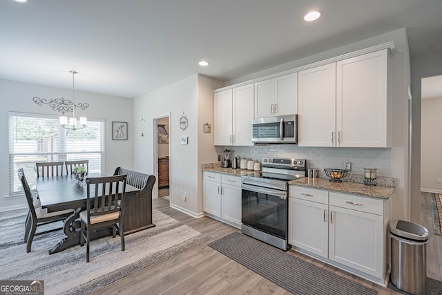 kitchen featuring stainless steel appliances, light wood-type flooring, backsplash, a chandelier, and white cabinets