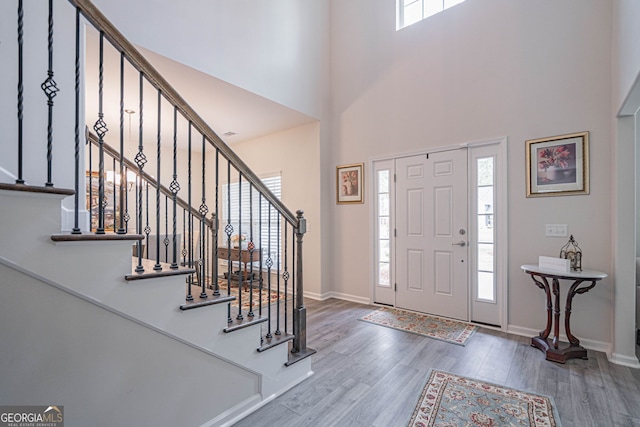foyer entrance featuring wood finished floors, stairs, baseboards, and a high ceiling