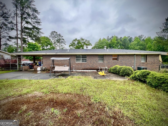 back of property with brick siding, an attached carport, driveway, central AC, and a yard