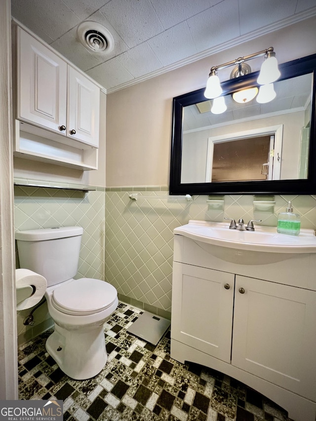 half bath featuring toilet, ornamental molding, vanity, wainscoting, and tile walls