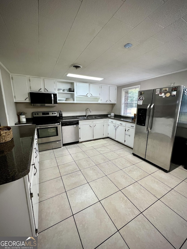 kitchen featuring appliances with stainless steel finishes, dark countertops, white cabinetry, a sink, and light tile patterned floors