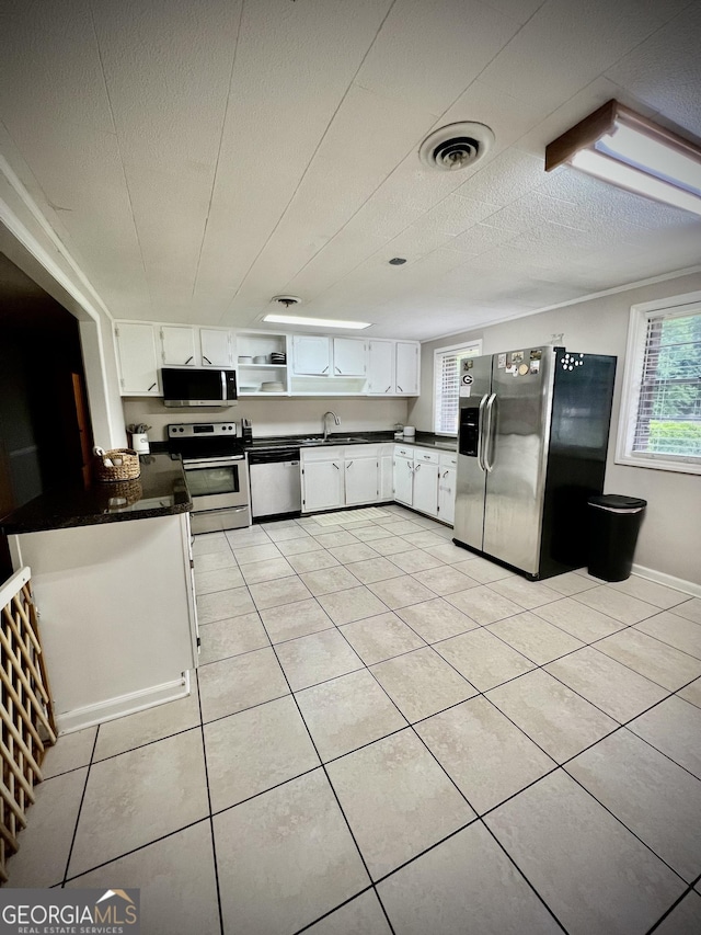 kitchen featuring appliances with stainless steel finishes, dark countertops, white cabinetry, and light tile patterned floors