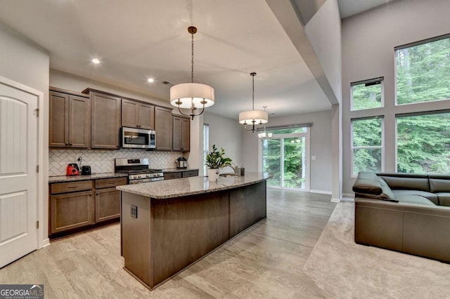 kitchen featuring stainless steel appliances, light stone countertops, light wood-type flooring, open floor plan, and tasteful backsplash