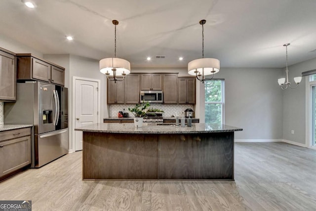 kitchen with appliances with stainless steel finishes, backsplash, stone counters, a sink, and baseboards