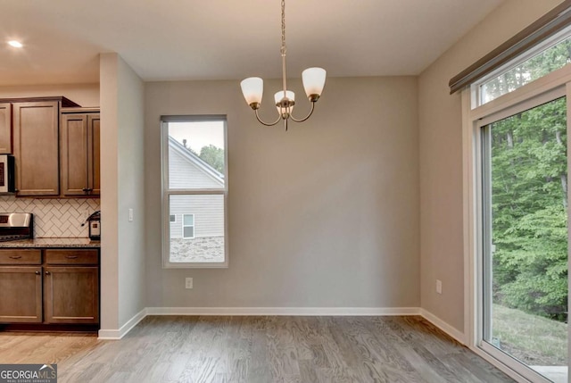 unfurnished dining area with light wood-style floors, a chandelier, and baseboards