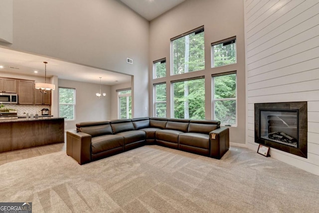 living area with a chandelier, a high ceiling, light colored carpet, a glass covered fireplace, and recessed lighting