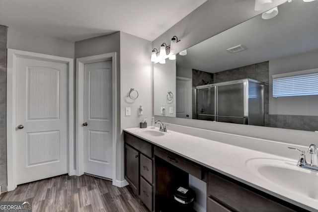 bathroom featuring a shower stall, double vanity, and wood finished floors