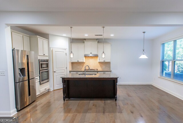 9872 Cameron Parc Cir, Johns Creek, GA 30022 - kitchen with stainless steel appliances, backsplash, light stone counters, wood finished floors, and pendant lighting