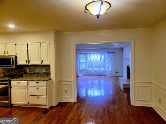 kitchen featuring stainless steel appliances, white cabinetry, dark wood-type flooring, ornamental molding, and wainscoting