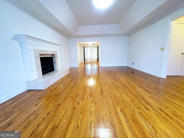 unfurnished living room featuring a raised ceiling, wood finished floors, baseboards, and a tiled fireplace