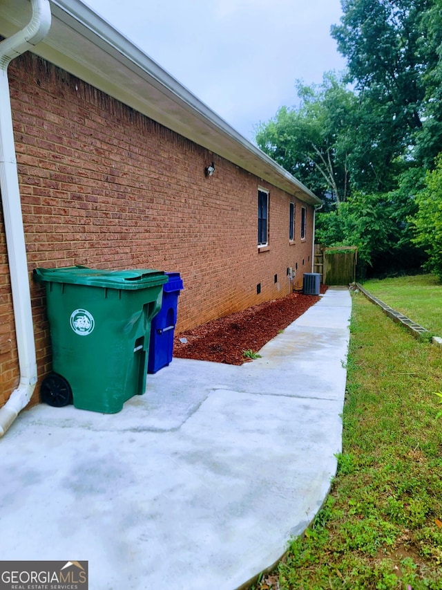 view of side of property with a patio, brick siding, and central air condition unit
