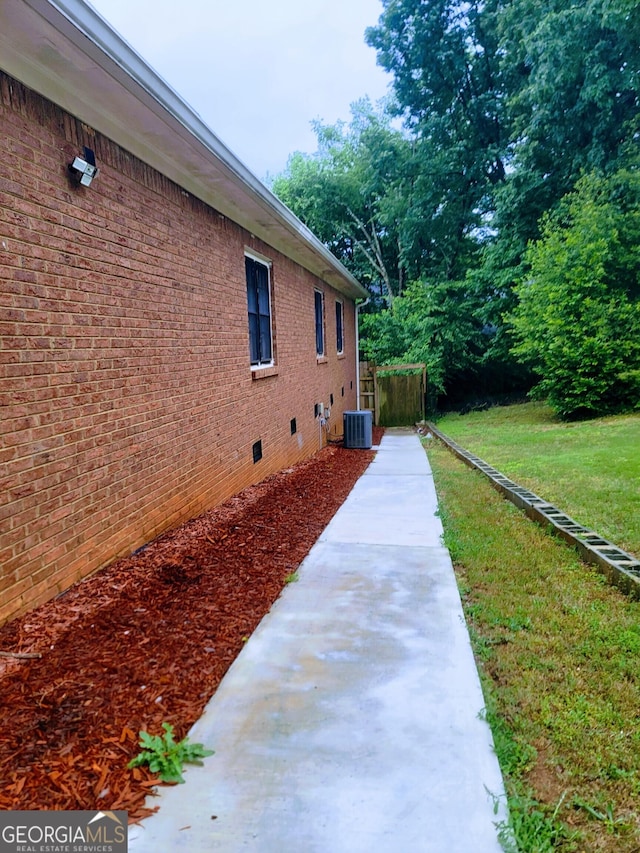 view of side of property featuring crawl space, a lawn, cooling unit, and brick siding
