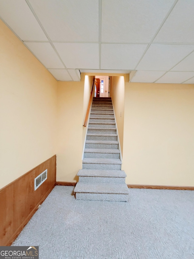 staircase with a drop ceiling, carpet, and baseboards