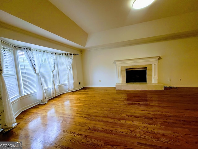 unfurnished living room with wood finished floors, vaulted ceiling, baseboards, and a tile fireplace