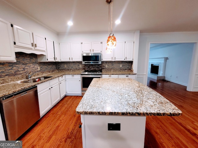 kitchen with stainless steel appliances, a sink, wood finished floors, backsplash, and ornamental molding