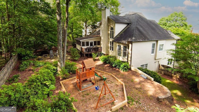 rear view of property with a chimney, fence, a deck, and a playground