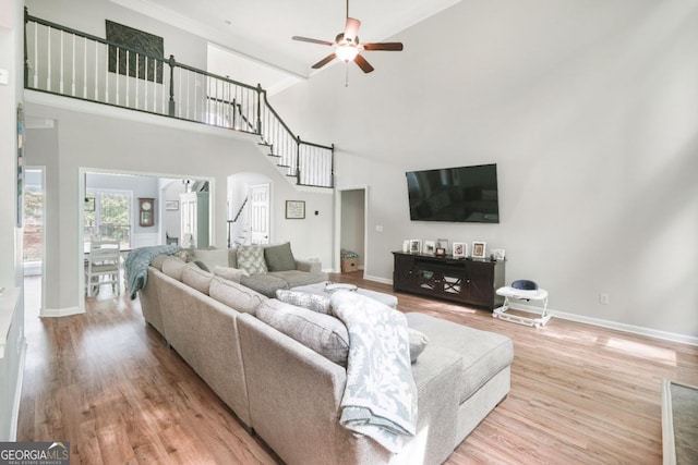 living area featuring high vaulted ceiling, a ceiling fan, stairs, wood finished floors, and baseboards