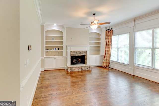 7520 Ledgewood Way, Suwanee, GA 30024 - unfurnished living room with ceiling fan, a stone fireplace, built in shelves, wood finished floors, and ornamental molding