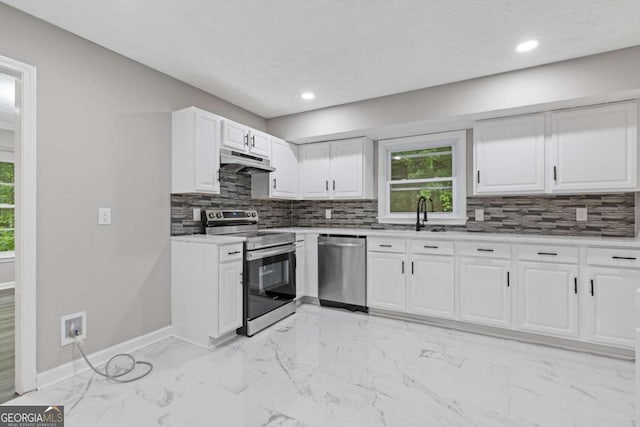 kitchen with stainless steel appliances, under cabinet range hood, a sink, backsplash, and baseboards