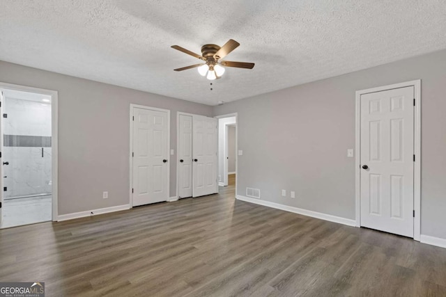 unfurnished bedroom featuring multiple closets, wood finished floors, baseboards, a textured ceiling, and connected bathroom
