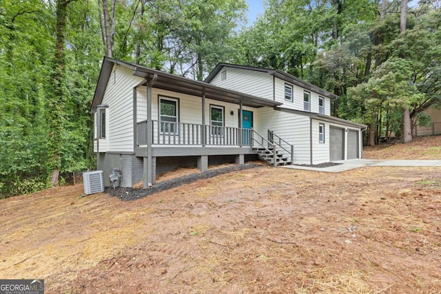tri-level home with a porch, driveway, an attached garage, central AC, and view of scattered trees