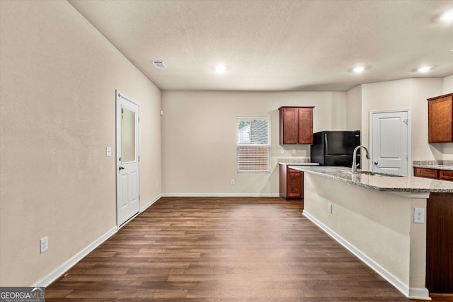 kitchen with freestanding refrigerator, a sink, dark wood-style flooring, baseboards, and light stone counters