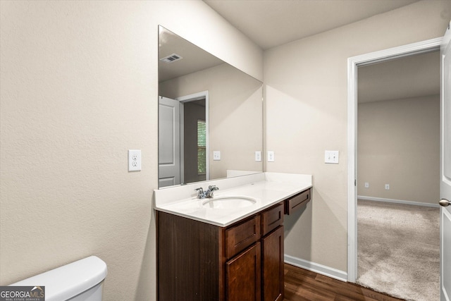 half bathroom with vanity, baseboards, toilet, and wood finished floors