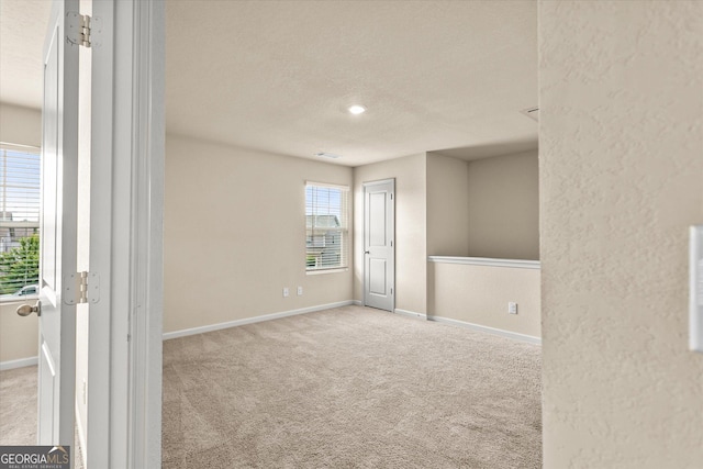 carpeted empty room featuring a textured ceiling, baseboards, and a textured wall