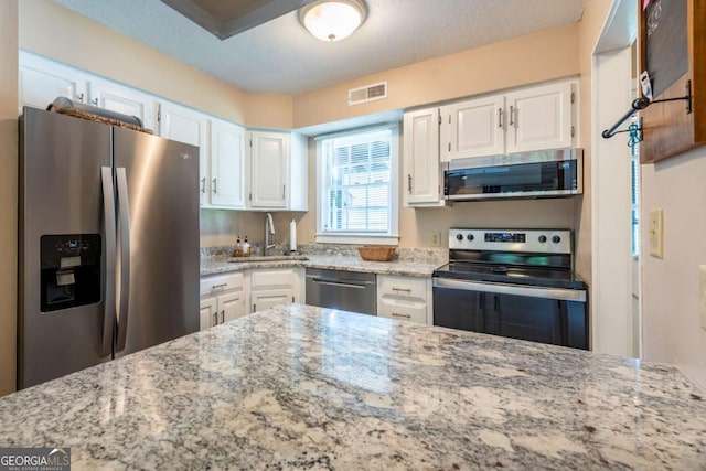 kitchen with appliances with stainless steel finishes, a sink, light stone counters, white cabinetry, and a textured ceiling
