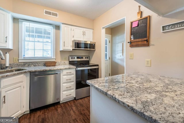 kitchen with appliances with stainless steel finishes, a sink, dark wood-style flooring, white cabinets, and light stone counters