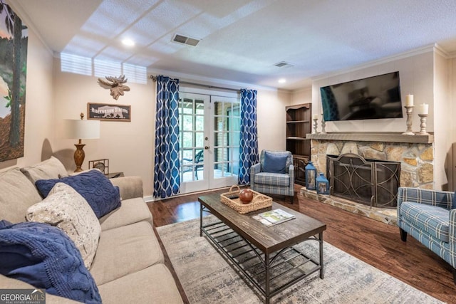 living room with crown molding, french doors, a stone fireplace, and wood finished floors