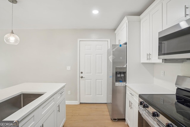 kitchen featuring appliances with stainless steel finishes, white cabinetry, light wood-type flooring, light countertops, and pendant lighting