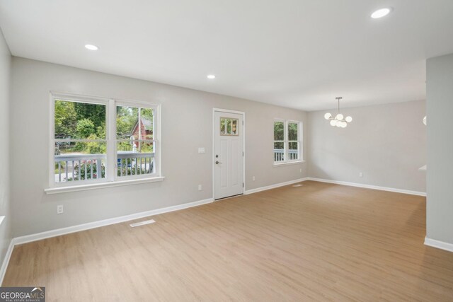 unfurnished living room featuring a chandelier, light wood-style flooring, baseboards, and recessed lighting