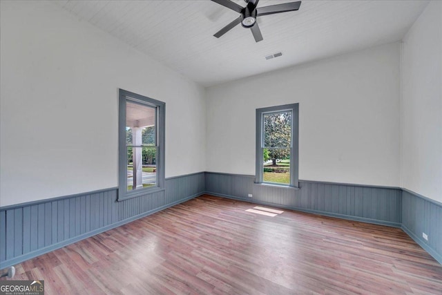 spare room with plenty of natural light, wood finished floors, wainscoting, and ceiling fan
